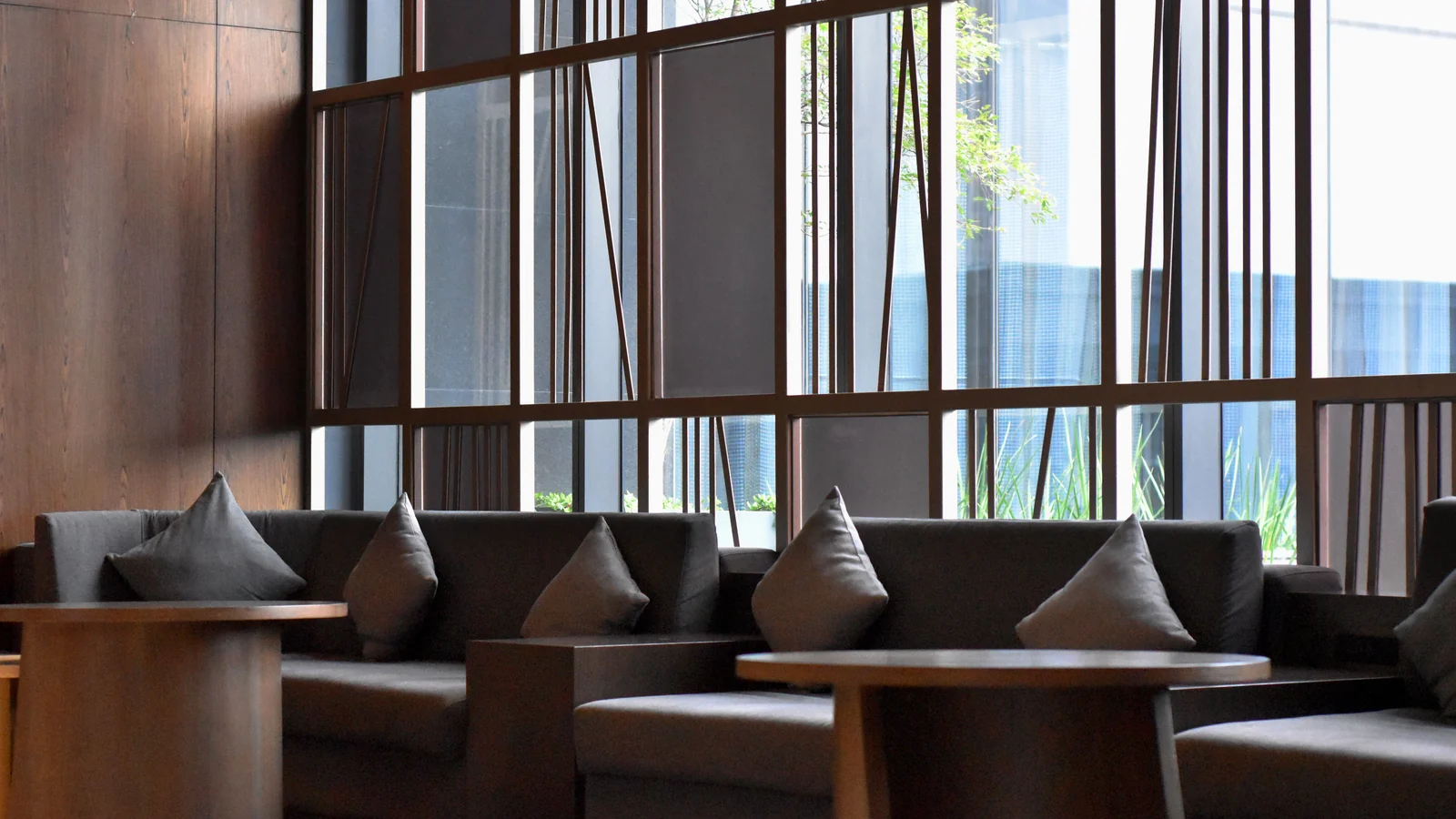 Illustrative stock image of lounge seating with cushions and low tables beside tall windows.