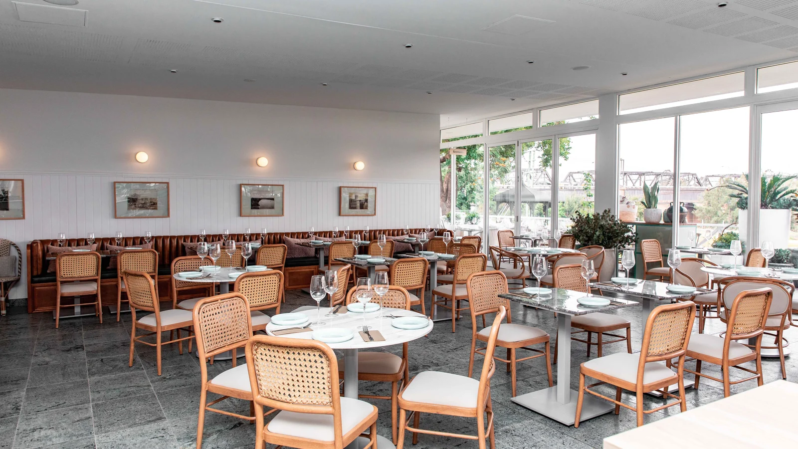 Illustrative stock image of a bright dining room with laid tables, wooden chairs and large windows.