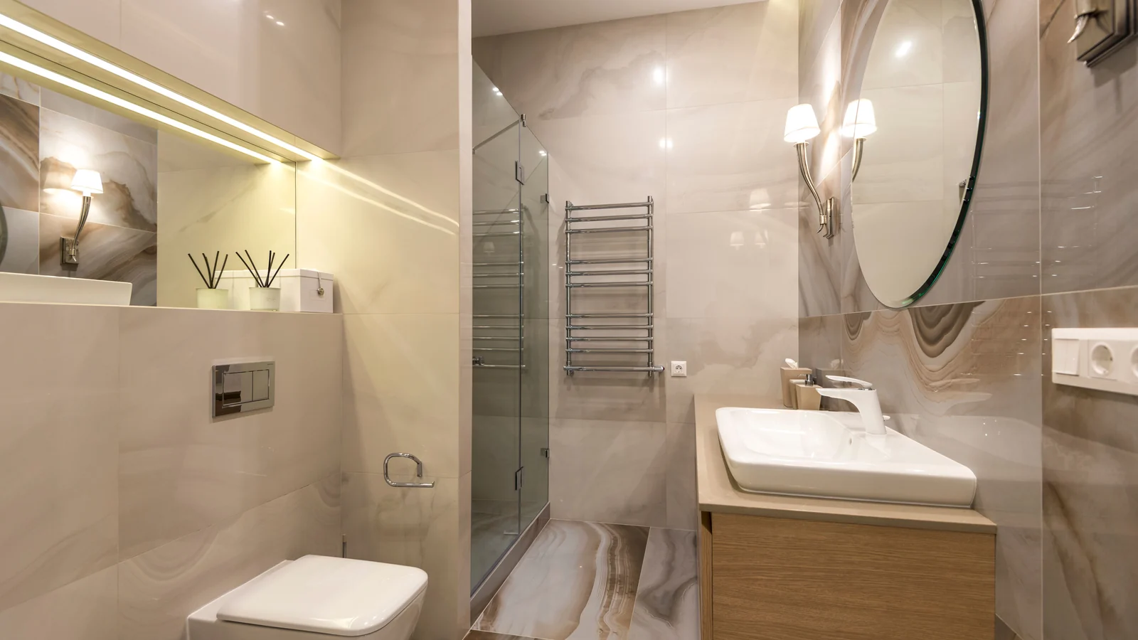Tiled bathroom with a glass shower enclosure, round mirror and basin.