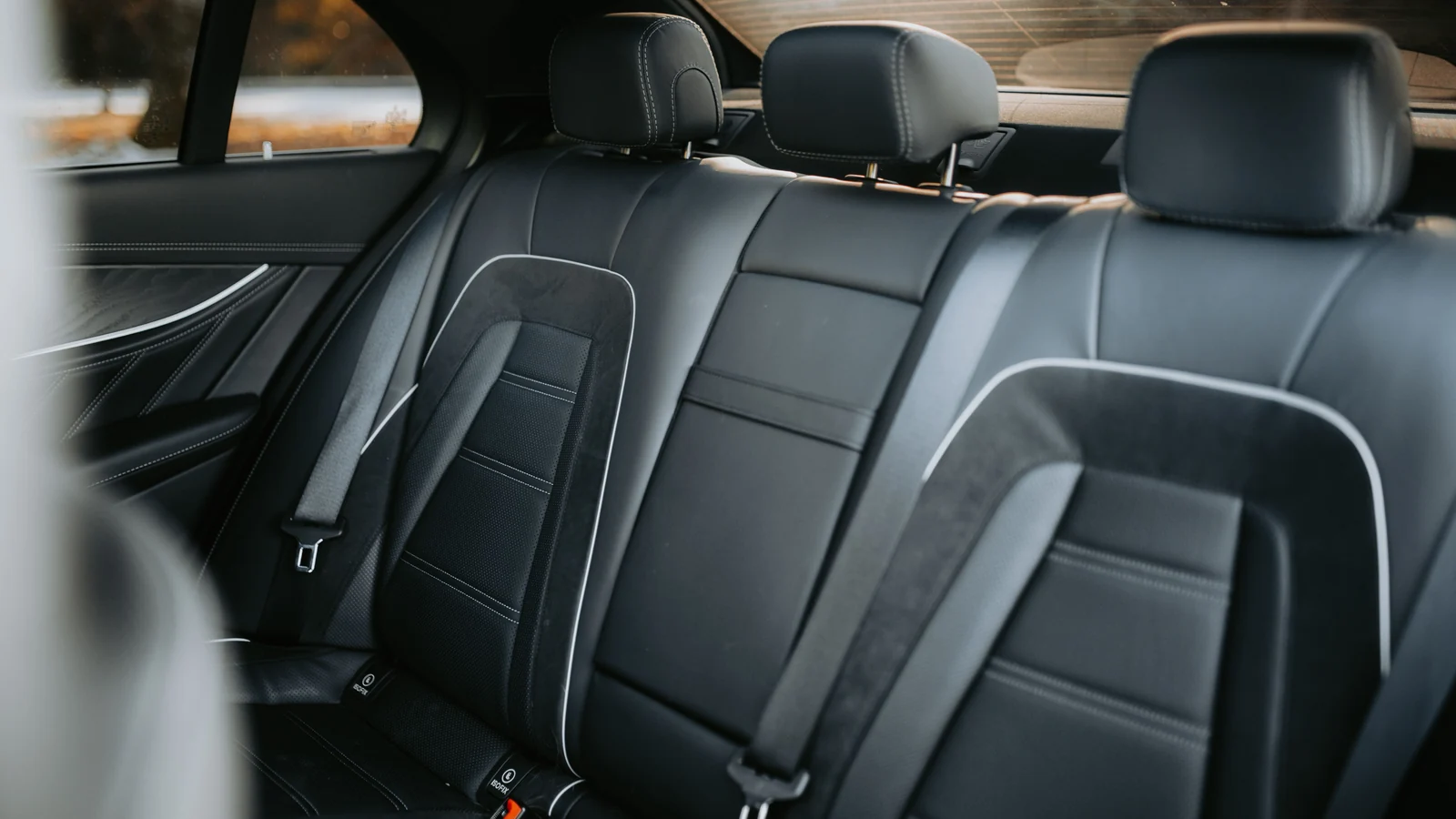 Black rear car seats with head restraints and seat belts.
