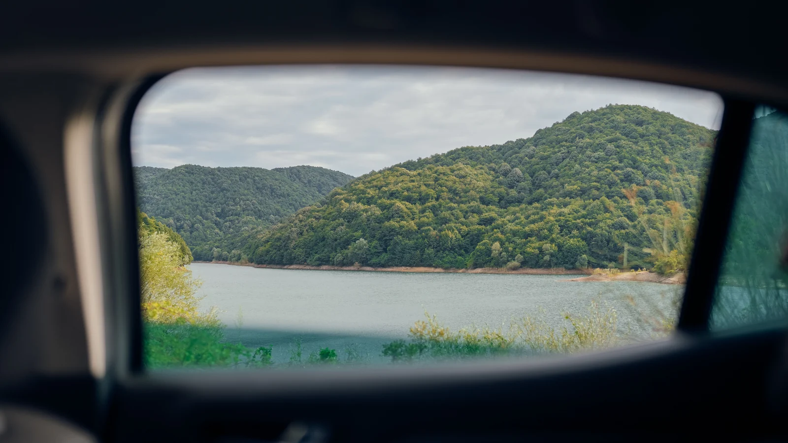 A lake and wooded hills seen through a car's side window.